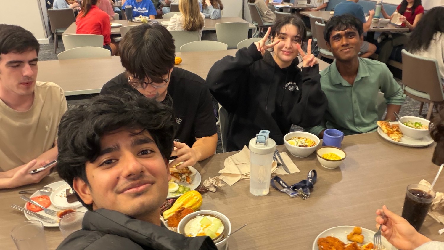 Aditya taking a selfie at a dining hall table with four friends.